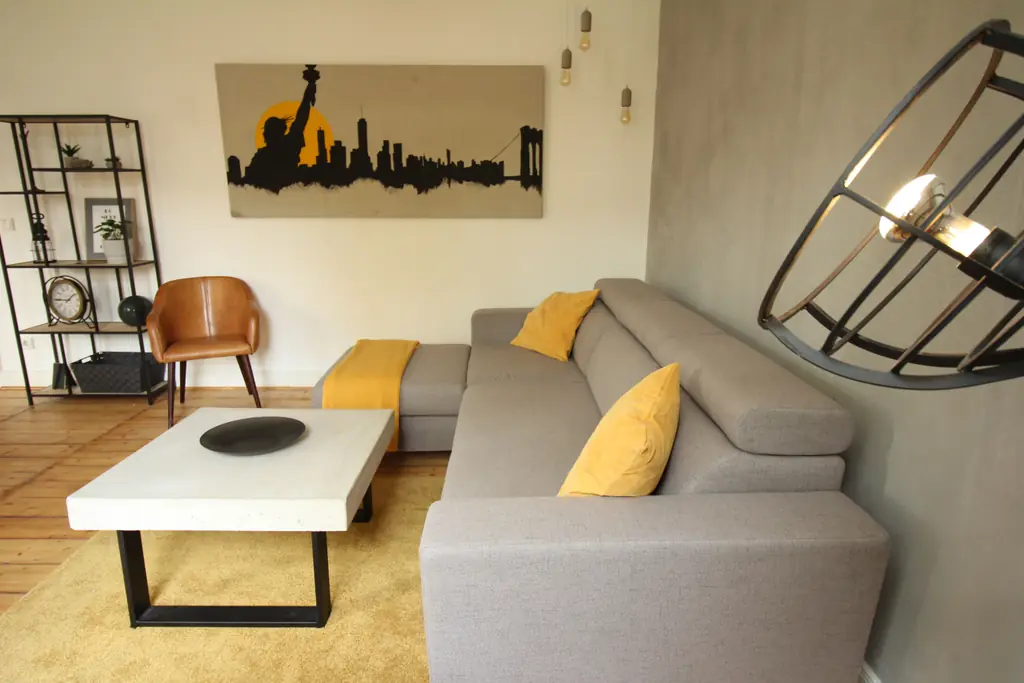 Wohnzimmer des NY Loft: graues Ecksofa, gelbe Kissen, Betonwand und Skyline-Bild